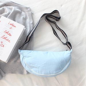 Flat lay of a light blue crescent crossbody bag with striped strap on white fabric