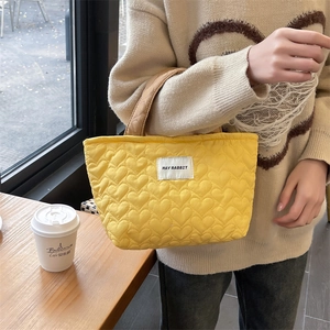 Detailed shot of yellow heart-quilted canvas handbag with branded label and brown handle