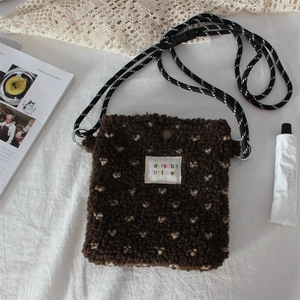 Detail of plush crossbody bag with heart pattern and woven strap on lifestyle background