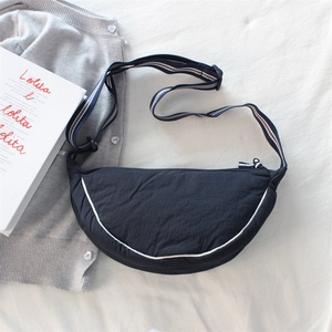 Flat lay of deep blue crescent bag with striped strap and contrasting white piping detail
