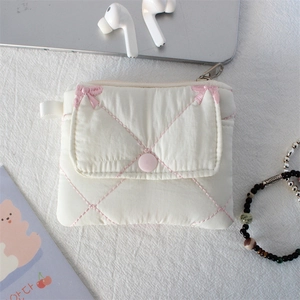 Detail of quilted card holder with bow embroidery and pink button closure on white desk