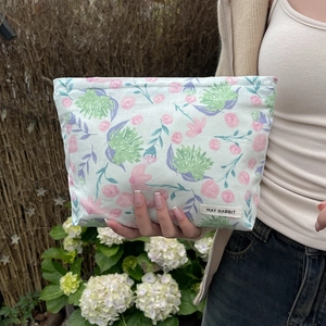 Floral makeup bag with May Rabbit label shown held against a garden background