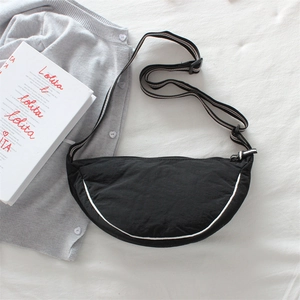 Close-up of black nylon dumpling bag with striped strap and white trim on fabric background