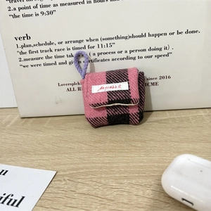 Detailopname van roze en zwarte tweed oortelefoonhoes met merklabel en draagkoord