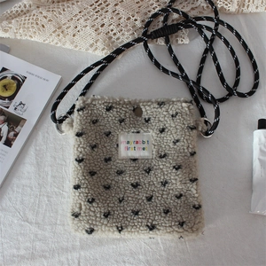 Detail of grey plush crossbody bag with black hearts and rope strap on white fabric