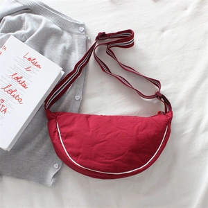 Detail of red dumpling bag with striped strap on sweater and book background