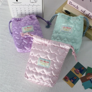 Close-up of heart-quilted satin drawstring bags in pastel purple, green, and pink