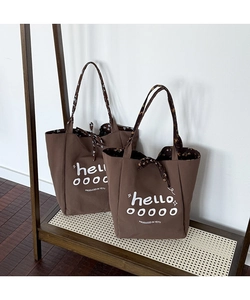 Detail of brown canvas tote bags with white artistic lettering and floral patterned straps