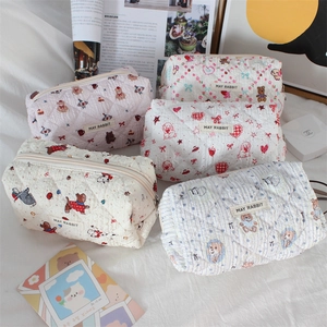 Detailed close-up of quilted cotton cartoon pouch set on a soft white bed sheet