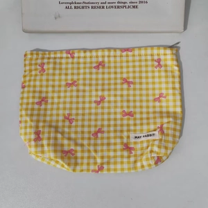 Close-up of yellow gingham pouch with pink bow patterns and a side brand label