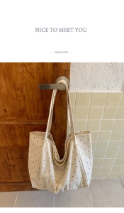 Close-up of beige canvas tote bag with black polka dots hanging on a wooden door handle