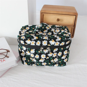 Close-up of embroidered daisy pattern on black quilted cosmetic bag with dual silver zippers