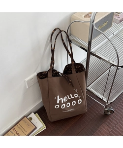 Detail of dark brown canvas tote bag with floral handles and hello print in home setting