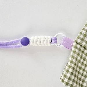 Close-up of woven shoulder strap and purple buckle on a green checkered crossbody bag