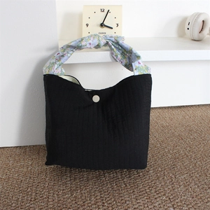 Detail of black pleated fabric bag with floral knot handle on a woven rug background