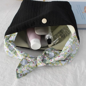 Detail view of the pleated black fabric tote bag with floral tie handles and metal snap closure