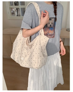 Close-up of beige canvas tote bag with black polka dots shown in a lifestyle indoor setting