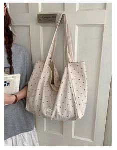 Close-up of a cream polka dot canvas tote bag with long straps hanging on a white wooden door