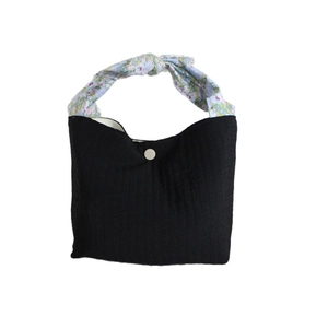 Minimalist black canvas tote bag with floral knot handles and white snap button closure