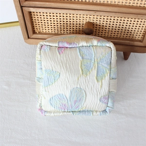 Detail of square floral pouch with butterfly print on pleated beige fabric texture