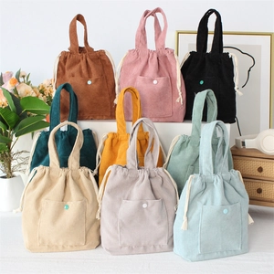 Corduroy drawstring handbags in various colors displayed on a minimalist wooden shelf