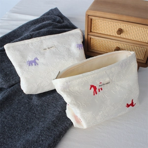Detail of satin jacquard makeup bags with horse embroidery and a textured fabric finish