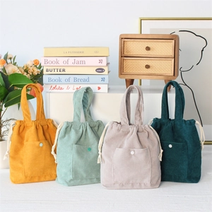 Detail view of corduroy drawstring handbags in yellow, mint green, and dark grey textures