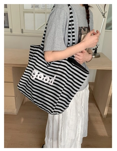 Detailed view of striped canvas tote bag featuring embossed 'good' lettering and wide strap