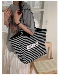 Detail of knit tote bag featuring black and gray stripes with bold white good lettering