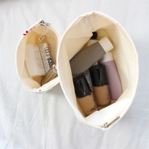 Detail view of large and small white canvas makeup bags with metal zippers and spacious interior