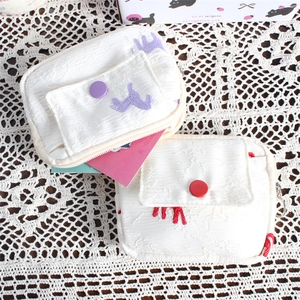 Detailed macro view of textured off-white coin purses with cute cat embroidery and button pocket