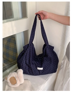 Close-up of navy blue polka dot canvas tote bag with woven logo label and wide strap