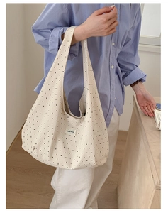 Close-up of cream canvas tote bag with black dots and embroidered lace brand label