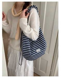 Detail of blue striped canvas tote bag showing ruffled strap and lace-trimmed logo patch