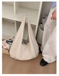 Close-up of a white canvas shoulder bag featuring a black polka dot pattern and cloth label
