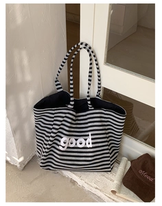 Detail of striped canvas tote bag with bold 'good' lettering against a clean wall