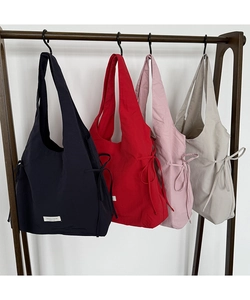 Four colorful nylon tote bags with side drawstring bows hanging on a wooden rack