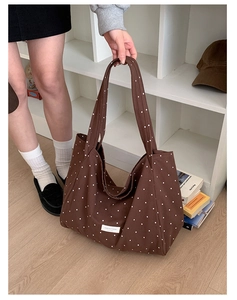 Detail of a brown polka dot canvas tote bag featuring a white label and long shoulder straps