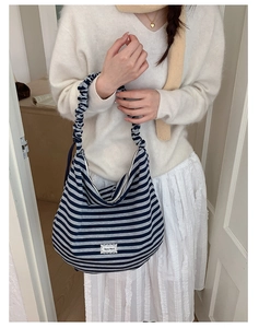 Detail of blue and white striped shoulder bag featuring pleated handle and Merci label
