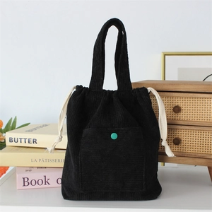 Detail of black corduroy handbag featuring a green button and white drawstring closure