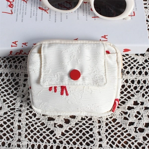 Detail view of a white jacquard mini pouch with a red button closure on a lace tablecloth