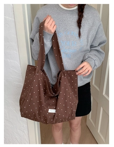 Detailed view of the brown polka dot canvas tote bag worn by a model in casual style