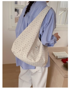 Close-up of beige canvas shoulder bag featuring black star patterns and woven side label