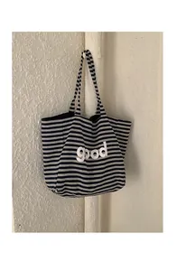 Detail of navy blue striped knit tote bag with white good letter print on textured wall