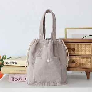 Detail of grey corduroy handbag with drawstring closure and front pocket on table