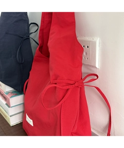 Detail of red nylon tote bag with side bow drawstring and white fabric brand label