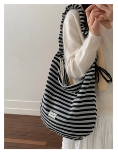 Detail of striped shoulder bag with ruffle strap, drawstring decor, and logo patch