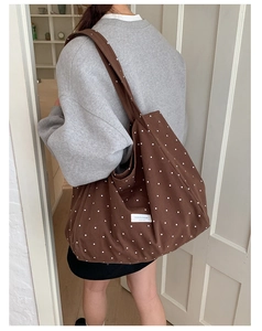 Detail of a brown polka dot canvas tote bag with a white square brand tag shown on a shoulder