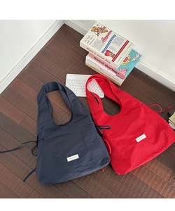 Flat lay of navy and red nylon tote bags with side drawstring and brand tag on wood floor