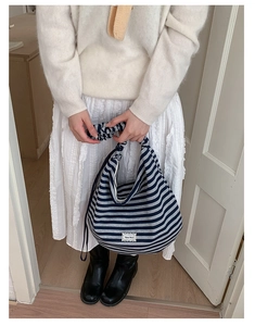 Detail of striped tote bag featuring ruffled handles and a lace-trimmed brand patch